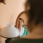Pani Barbara ubrana w zielony żakiet spogląda w lustro z lekkim uśmiechem.
