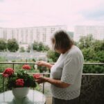Pani Renana stoi na balkonie i dotyka kwiatów w doniczce.